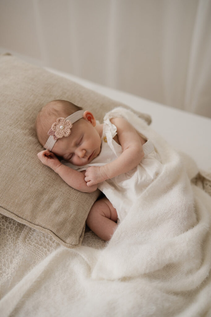 Ein Baby trägt ein zartes Blumenstirnband und schläft auf einem Kissen beim Newbornshooting in Dachau
