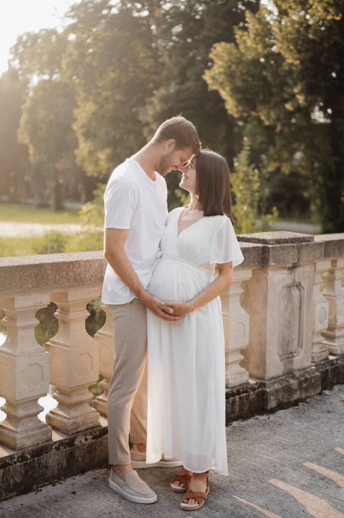 Ein junges Paar steht auf einer Brücke beim Sonnenuntergang beim Babybauchshooting