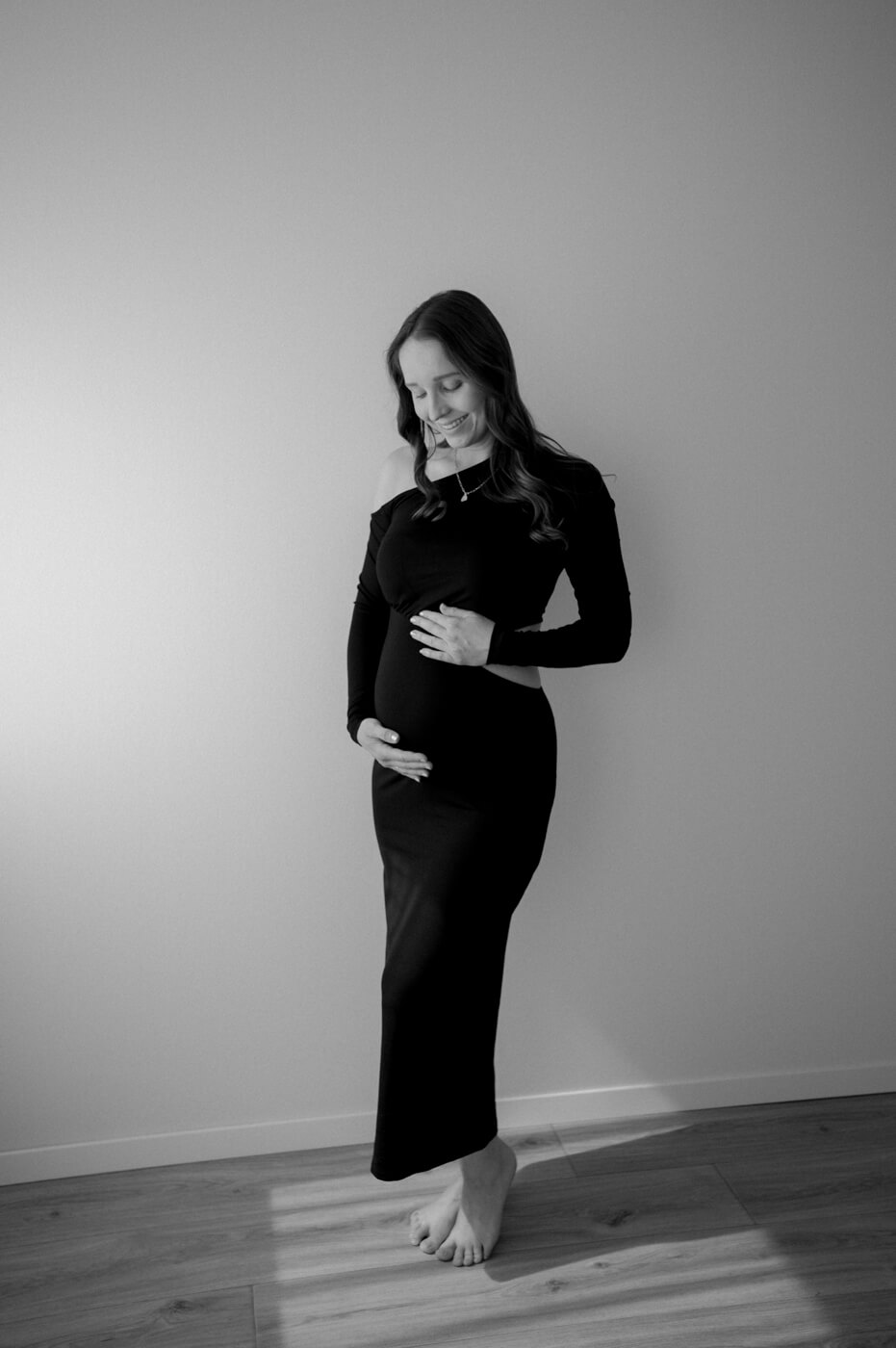 Eine schwangere Frau steht in einem schwarzen Kleid in einem Fotostudio in Dachau beim Babybauchshooting.