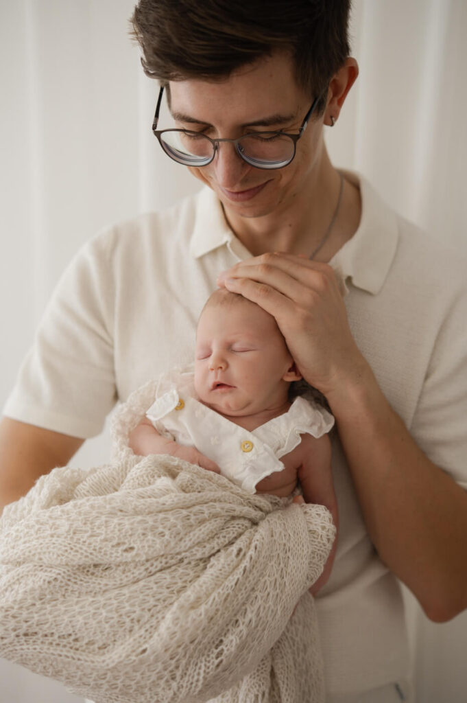 Ein Vater hält seine neugeborene Tochter beim Newbornshooting im Arm
