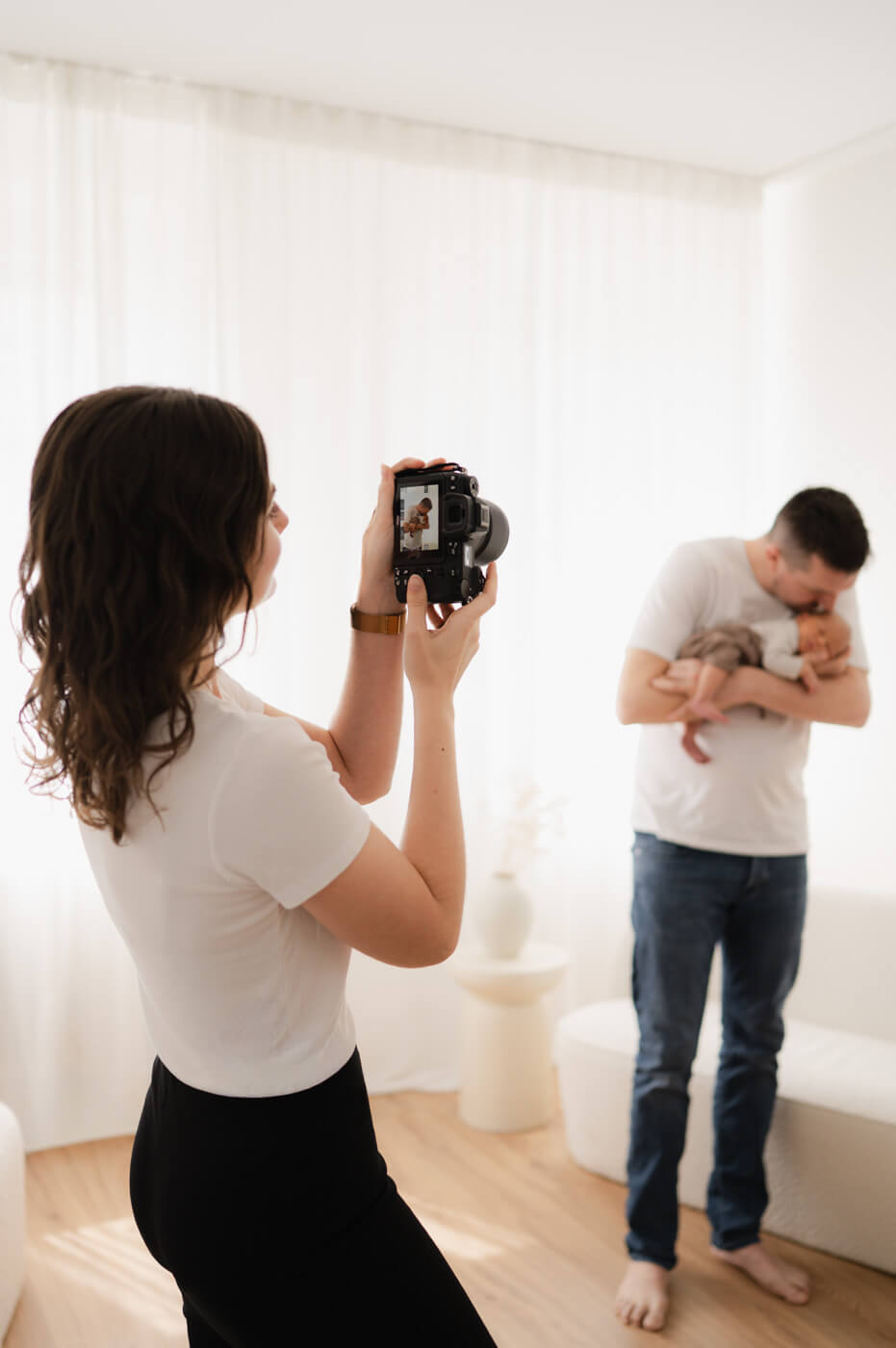Eine Fotografin in ihrem Studio fotografiert einen Mann mit Baby beim Newbornshooting