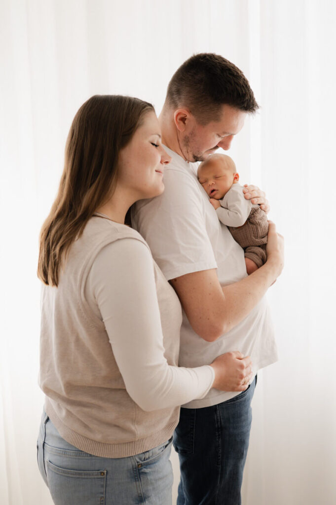 Mama, Papa und Baby stehen vor einem weißen Vorhang beim Neugeborenenshooting in Dachau.